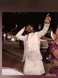 a man in a white jacket is dancing in front of a drum with his arms in the air