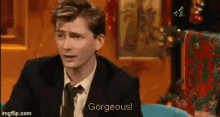 a man in a suit and tie says gorgeous while sitting in a chair