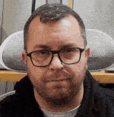 a man with glasses and a beard looks at the camera