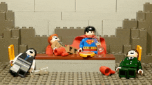 three lego figures are sitting around a table with one of them wearing a superman outfit