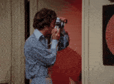 a man in a blue shirt is taking a picture with a camera that says ' nikon ' on the front