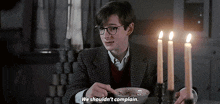 a boy with glasses is sitting at a table with candles and a bowl of cereal .