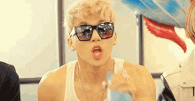 a young man wearing sunglasses and a tank top is holding a blue balloon .