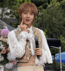 a young man in a costume is holding a microphone and pointing at his face .