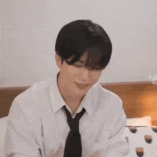 a man in a white shirt and tie is sitting on a bed eating a cupcake .