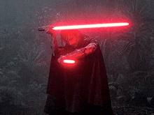 a man in a black cape is holding a red light saber in the dark .