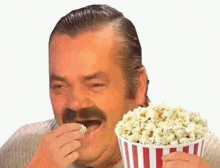 a man with a mustache is eating popcorn from a striped container .