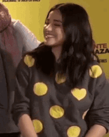 a woman wearing a polka dot sweater with yellow hearts on it is smiling .