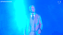 a man in a suit and tie is standing in front of a blue light with the hashtag thekamdreesen
