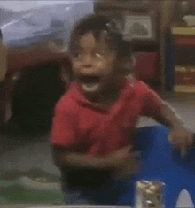 a little boy in a red shirt is sitting in a blue chair with his mouth open .