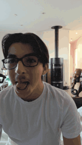 a young man wearing glasses and a white t-shirt is sticking his tongue out