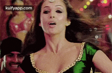 a woman in a green and gold dress is dancing in front of a crowd .