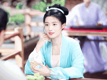 a woman in a blue dress sits at a table with a cup of tea