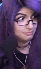 a woman with purple hair and glasses is wearing headphones .