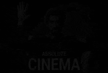 a man in a suit is sitting in a chair with his hands in the air and the words absolute cinema below him