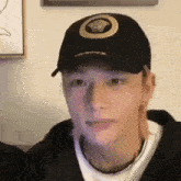a young man wearing a black baseball cap and a white shirt is looking at the camera .