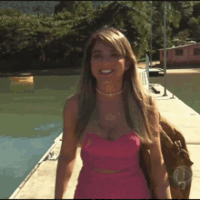 a woman in a pink dress stands on a dock