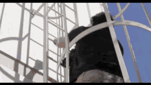 a man climbs up a metal ladder with a blue sky in the background