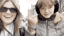 two girls wearing ear muffs and sunglasses are standing next to each other on a sidewalk .