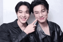 two young men wearing leather jackets and glasses are posing for a picture together .