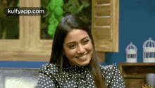a woman in a black and white polka dot shirt is smiling and sitting on a couch .