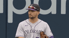 a baseball player wearing a purple uniform and a black hat is holding a glove .