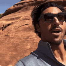 a man wearing sunglasses stands in front of a rock
