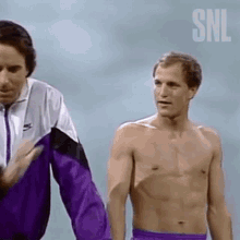 a shirtless man in purple shorts is standing next to another shirtless man .
