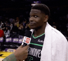 a basketball player with a towel around his neck is being interviewed by a tv reporter