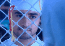a man behind a chain link fence wearing a bandana
