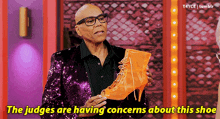 a man in a sequined suit is holding an orange shoe and says the judges are having concerns about this shoe .