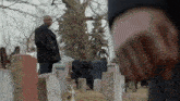 a man in a black coat is standing in a cemetery with a crowd of people .