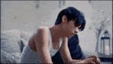 a young man wearing a white tank top is sitting on a couch