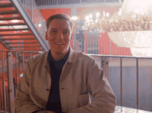a man in a tan jacket sits in front of stairs