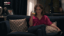 a woman sits on a couch with a glass of orange juice in front of a tv screen that says na corsa gamba