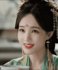 a woman with a red flower on her forehead is smiling while holding a cup