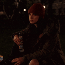a woman wearing a red beanie is holding a bottle of alcohol