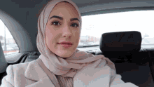 a woman wearing a hijab and a white coat is sitting in the back seat of a car