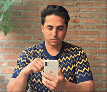 a man wearing a blue and yellow sweater looks at his phone