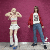 a man and a woman are standing next to each other and dancing in front of a pink wall .