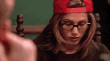 a woman wearing glasses and a red hat is looking at another woman .