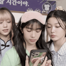 three girls are looking at a cell phone with a sign behind them that says ' a ' on it