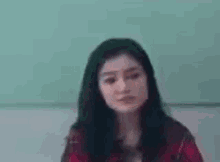 a young woman in a plaid shirt is sitting in front of a green wall .