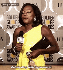 a woman is holding a trophy and talking into a microphone at the golden globe awards .