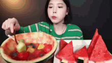 a woman in a green striped shirt is eating a bowl of watermelon and fruit