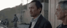 two men are standing next to each other in front of a building and looking at each other .