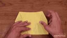 a person is folding a piece of yellow paper with the words made in animatica visible