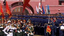 a group of soldiers marching in front of a pink building with a flag that has the letter a on it