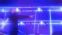 a man in a black jacket is pointing at something in a dark room with blue lights