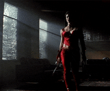 a woman in a red outfit is holding a sword in a dark room